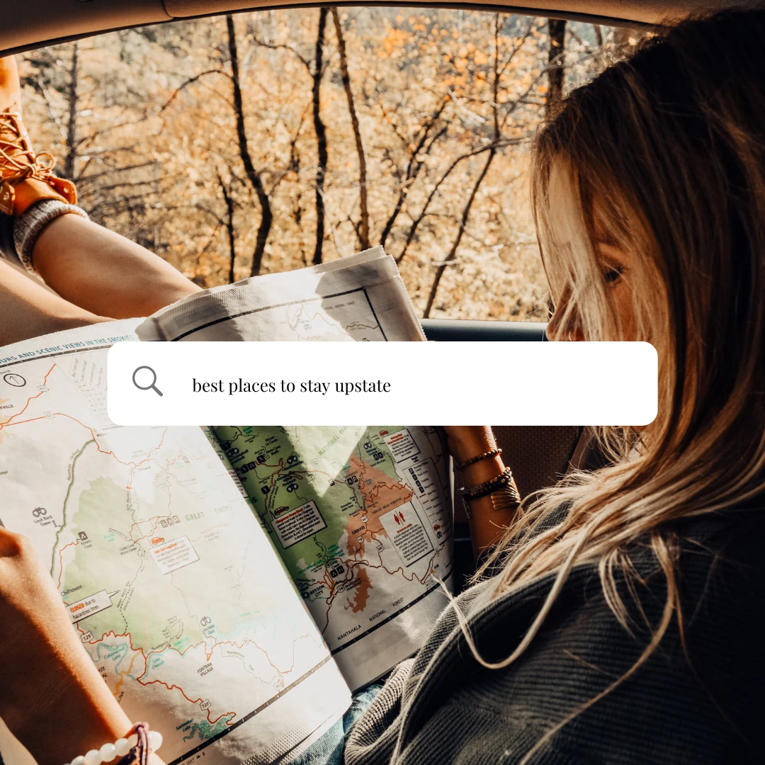 A woman in a car reading a trail map, under a search bar that reads “best places to stay upstate”